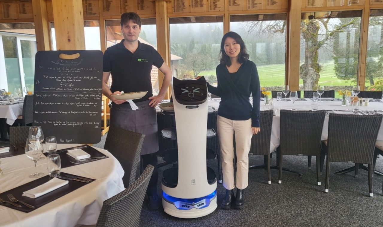 Fabian et Keunhyung Cho Adam au côté de Bella, une nouvelle serveuse au top de la technologie. (Photo : Restaurant du Golf Les Bois)
