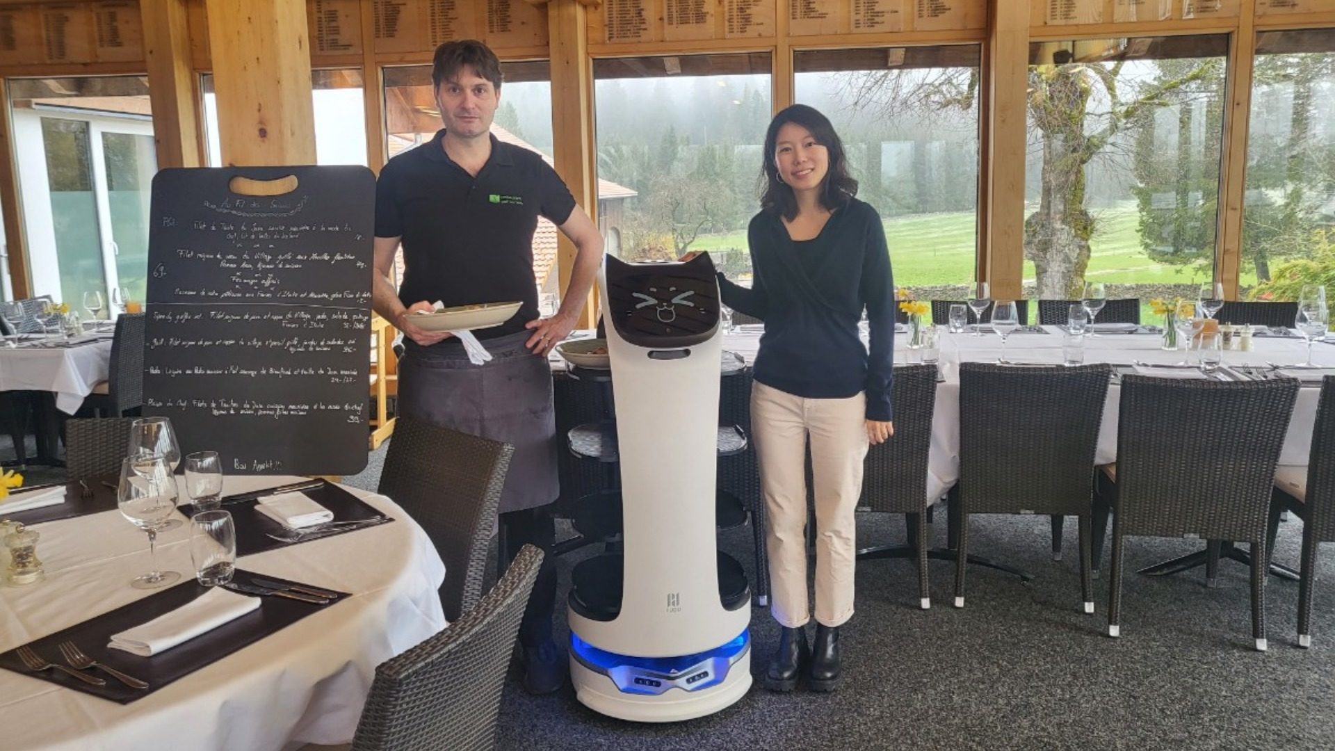 Fabian et Keunhyung Cho Adam au côté de Bella, une nouvelle serveuse au top de la technologie. (Photo : Restaurant du Golf Les Bois)